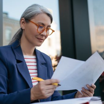 Pensive mature businesswoman reading contract, planning project, brainstorming. Portrait of attractive asian secretary reading, working with documents, sitting at workplace